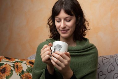 Kanepede elinde kahve tutan bir kız.