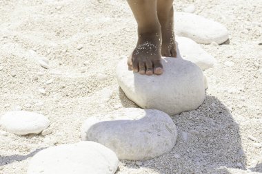 Yaz tatili boyunca kumlu bir plajda oynayan ve beyaz taşların üzerinde duran küçük bir çocuğun çıplak ayaklarına yakın çekim görüntüsü..
