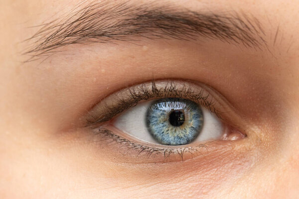 A closeup view on the blue iris and eye of a thirty something Caucasian lady. Pretty girl with minimal makeup looks into a macro lens. Detailed vision and beauty concepts