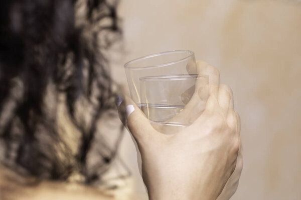 Closeup view of woman's shaking hand holding drinking glass suffering from Parkinson's disease