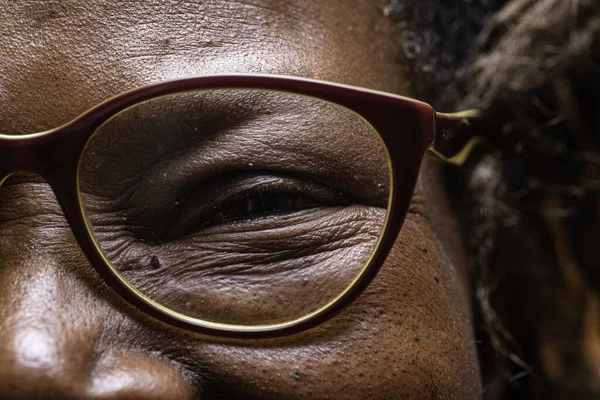 An extreme closeup view on the eye of an elderly African woman wearing reading glasses, jovial and smiling wise old woman in close-up detail.