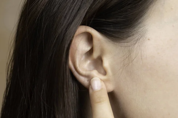 A closeup and side profile view of a hard of hearing girl, using finger to point towards the ear, hand gesture of disabled girl struggling to hear conversation.