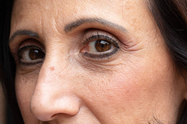 A closeup view on the eyes and face of a Caucasian lady in her late forties. Wearing black eyeliner and mascara with crows feet and skin imperfections