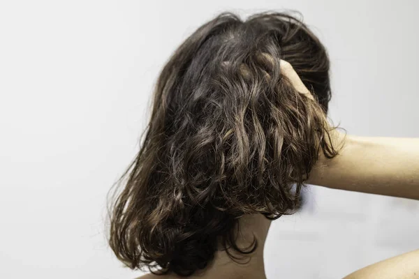 A beautiful brunette woman with shoulder length wavy hair is seen up close from the back, isolated against a white background as she runs fingers through hair with copy space.