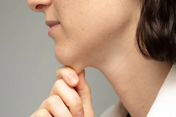 A close up and side profile view of a young Caucasian lady pinching the skin beneath her jaw. Self-conscious about her appearance and body fat.