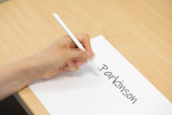 A close-up and burry view of a woman trying to write on white paper with tremors. Person with Parkinsons disease struggles with daily activities