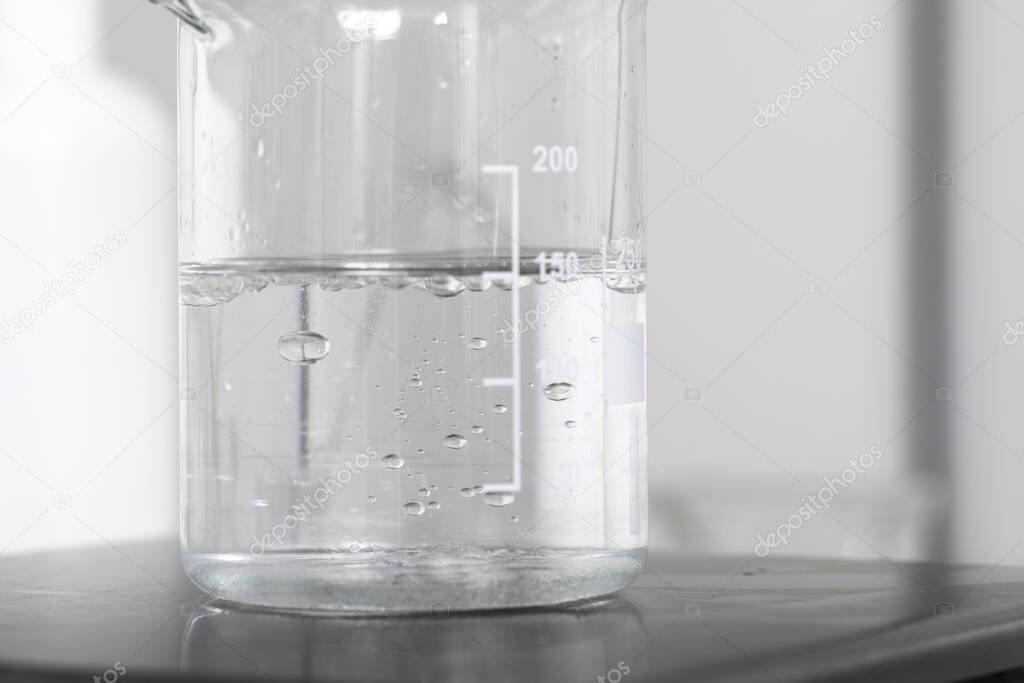 Beaker with water, clear liquid in lab mixer close up