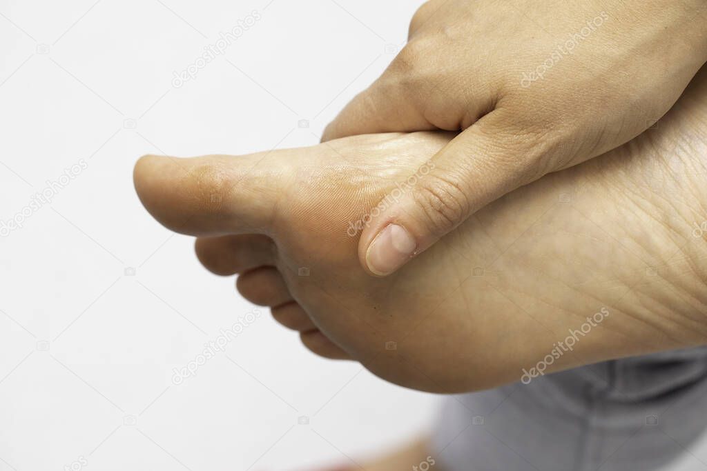 A closeup view on the foot of a person with a busy lifestyle, tired and aching, using hand to rub the underside of the sole and big toe, isolated against a white background.
