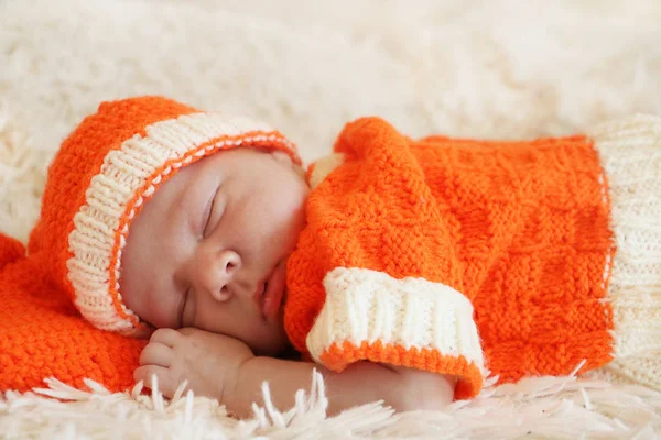 Cute sleeping newborn baby dressed in a knitted orange costume o