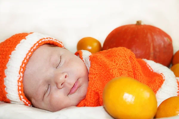 Милый спящий улыбающийся новорожденный ребенок, одетый в вязаный апельсин — стоковое фото