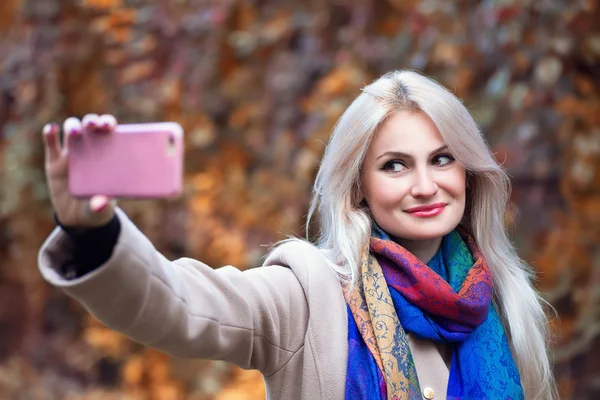 Young blonde woman taking selfie in park in autumn — Stock Photo, Image