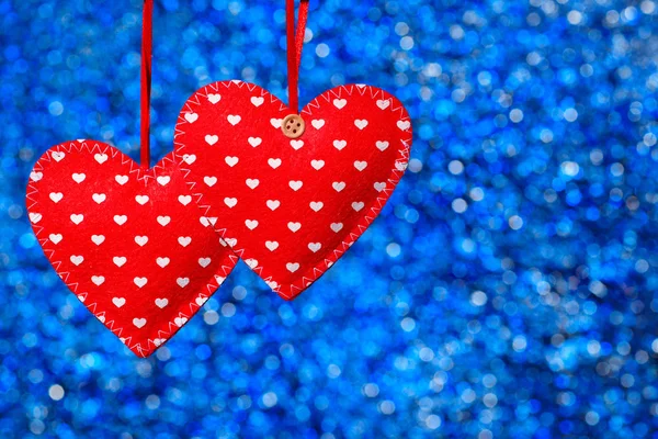 Dwa czerwone serca szyte wiszące na niebieskim tle — Zdjęcie stockowe