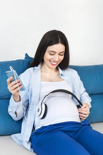 Mujer embarazada sosteniendo auriculares en su vientre — Foto de Stock