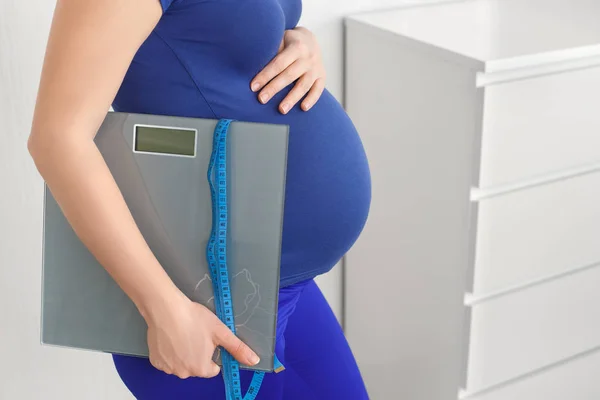 Mujer embarazada sosteniendo escamas cinta métrica — Foto de Stock