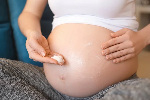 Zwangere vrouw aanbrengen crème op haar buik — Stockfoto