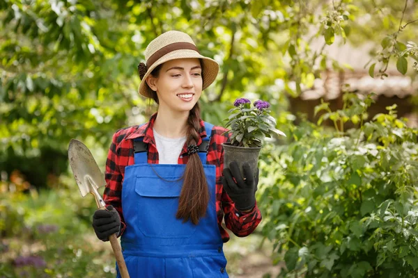 Садівник в робочому одязі тримає квітку в горщику і дрібну ложку — стокове фото