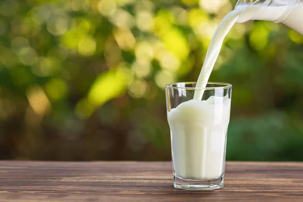 Milk from jug pouring into glass — Stock Photo, Image