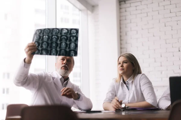 Team of three doctors discuss X-ray of patient in consulting room of hospital