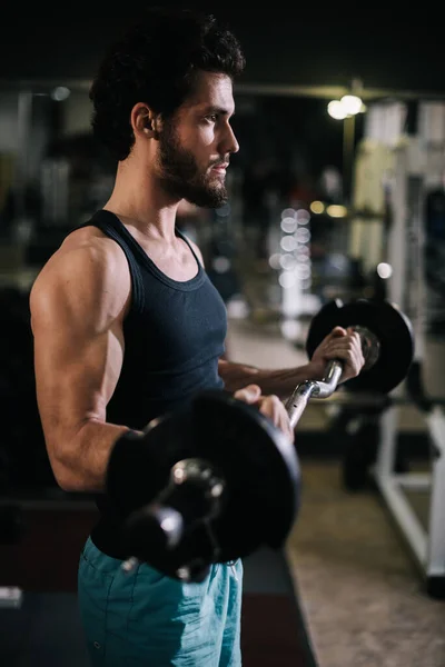 Side view of sportive bearded young man with muscular body working out with barbell