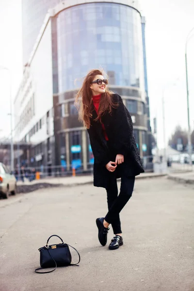 Hübsches Mädchen mit langer Frisur und roten Lippen in Sonnenbrille läuft mit einer Tasche auf der Straße. sie lächelt und sieht genüsslich aus. — Stockfoto