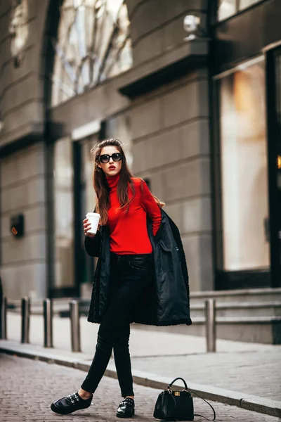 Windows.Wearing moda gözlük ve siyah bir ceket tarafından geçen genç şık kız. Kahve tutan.