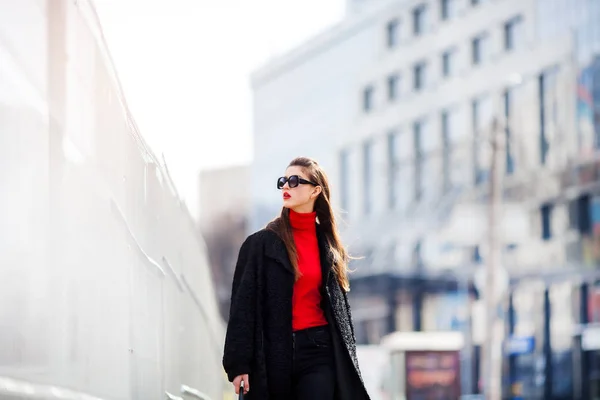 Jeune femme à la mode marchant dans la rue dans la ville Elle porte des lunettes de soleil, chemise noire et veste  . — Photo