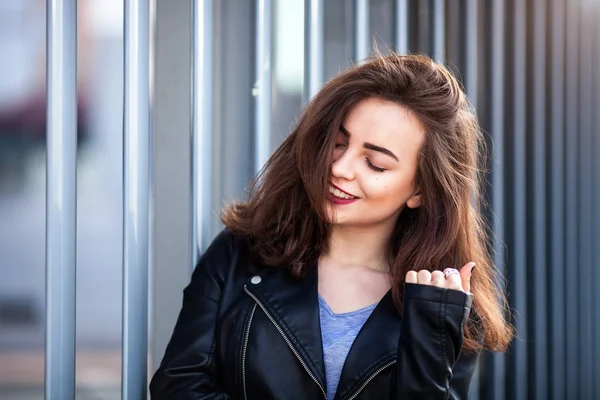 Fantastiska glada vackra flicka med lång brunett hår. poserar utomhus. skinnjacka, brunett hår, röda läppar nära upp mode gatan stile porträtt — Stockfoto