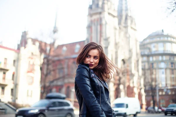 Junge schöne Brünette zu Fuß durch die Stadt.Lederjacke, urbaner Rucksack, leuchtend rote Lippen das Konzept der Straßenmode. — Stockfoto