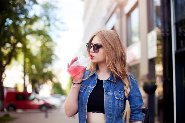 Adorable fille dans un costume de denim à la mode avec une coiffure longue et lèvres rouges boire limonade rafraîchissante — Photo