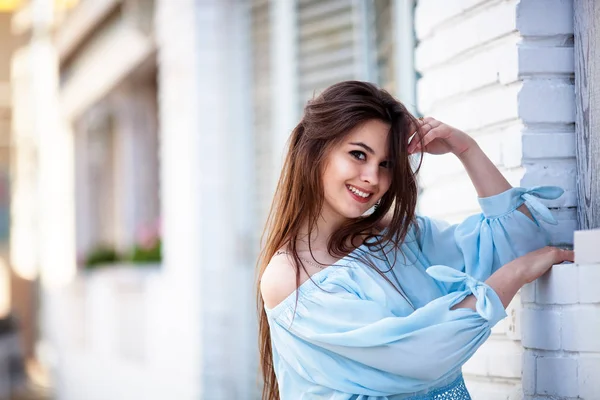 Primer plano de chica morena atractiva con el pelo largo de pie cerca de la cafetería. Lleva una blusa azul con los hombros abiertos — Foto de Stock