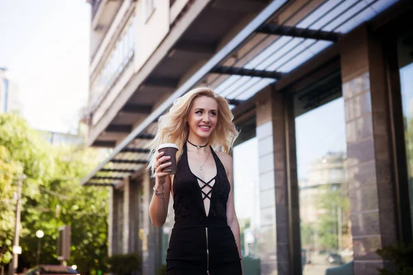 Close-up Fashion portrait of a young pretty fashionable girl posing in a city in Europe, summer street fashion, holding a coffe laughing and smiling