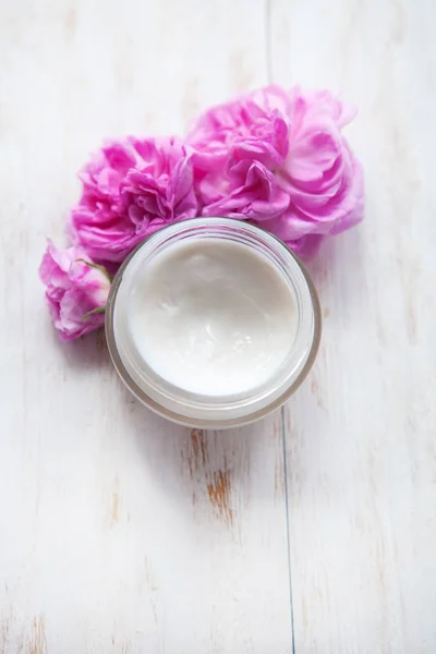 Maceta de crema de belleza rodeada de flores sobre mesa de madera blanca Cosméticos para el cuidado — Foto de Stock