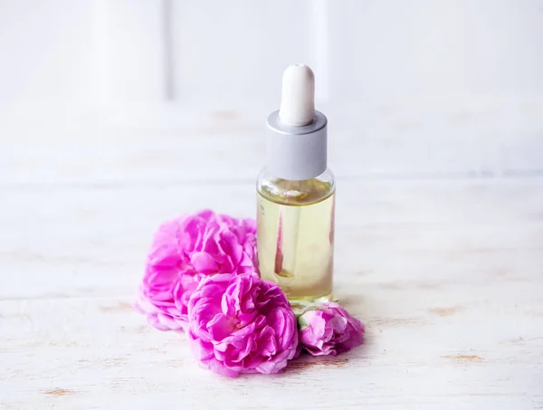 Biologische cosmetica met roos olie omringd door bloemen op witte houten tafel — Stockfoto