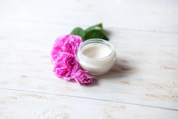Pot of beauty cream surrounded by flowers on white wooden table — Stock Photo, Image