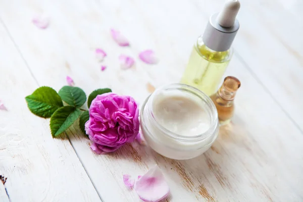 Spa setting with pot of moisturizing face cream beautiful pink roses and rose essence oil on white background — Stock Photo, Image