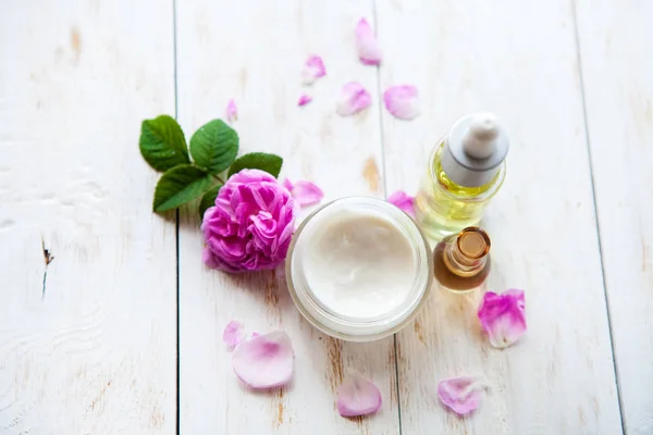 Spa concept with pot of moisturizing cream beautiful pink roses and rose essence oil on white wooden background Spa treatment. — Stock Photo, Image