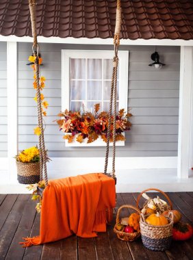 Veranda of countryside house in autumn season. swing is adorned with autumn leaves and orange knitted plaid. Basket with pumpkins and autumn vegetables. window is decorated with autumn decor. clipart