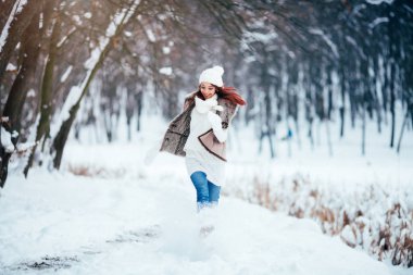 Kız bir kürk yelek giymiş ve beyaz bir kazak karla kaplı yolda çalışır.