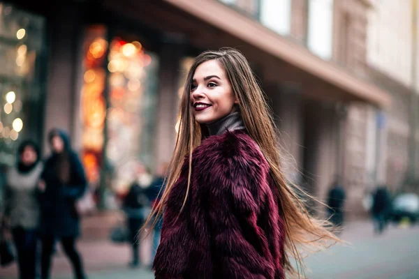 Young beautiful model girl smiles and looks back in the city. Dynamically young girl walks down the street.Hair fluttering in the wind. — Stock Photo, Image