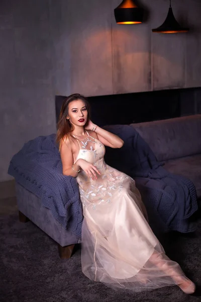 Vogue fashion style portrait of young beautiful pretty elegant rich woman wearing evening dress near armchair in luxury apartments.