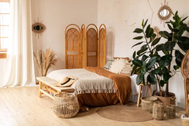 Modern ev iç tasarımı. Beyaz ve bej battaniyeler, boho yatak odasının iç kısmı, egzotik yatak odası iç kısmı, İskandinav tarzı. Dokulu duvarlar, ahşap zemin, güneşli gölgeler, doğal malzemeler, saman ekran.