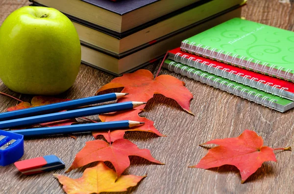 Books, pencils, notebooks, autumn red leaves and green apple