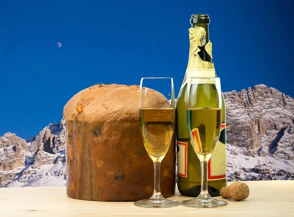 Klasik İtalyan Noel kek panettone ile kurutulmuş meyve ve iki bardak şarap şişe. Arka plan Dolomites dağlar. — Stok fotoğraf