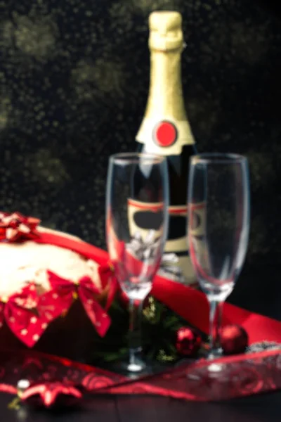 Bulanık arka plan: Noel ve yeni yıl. Şampanya gözlük mumlar, panettone ve kırmızı saten fiyonklu hediye paketi. Boşluk. Festival kavramı — Stok fotoğraf