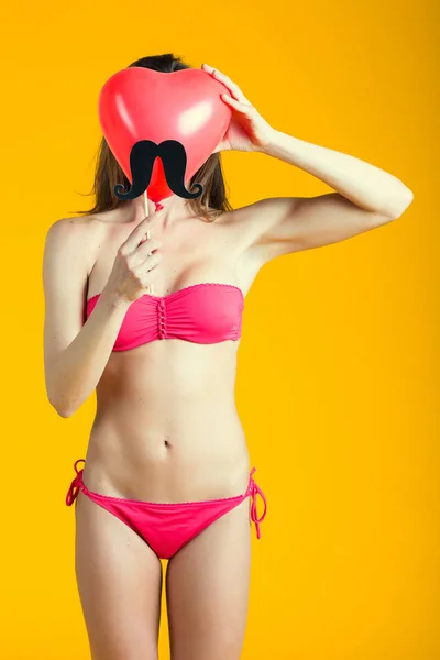 Hermosa mujer morena en bikini rosa jugando con globo en forma de corazón rojo —  Fotos de Stock
