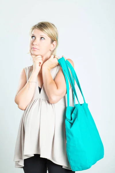 Beautiful pensive young blonde pregnant woman with shopping bags posing. Pregnancy, motherhood, sale, people and expectation concept. Isolated on background.
