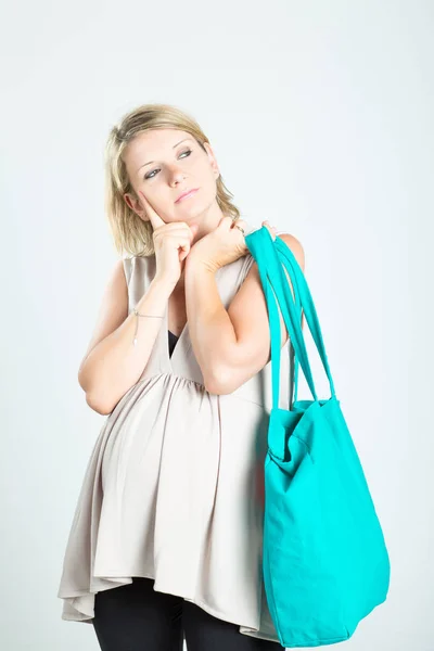Beautiful pensive young blonde pregnant woman with shopping bags posing. Pregnancy, motherhood, sale, people and expectation concept. Isolated on background.