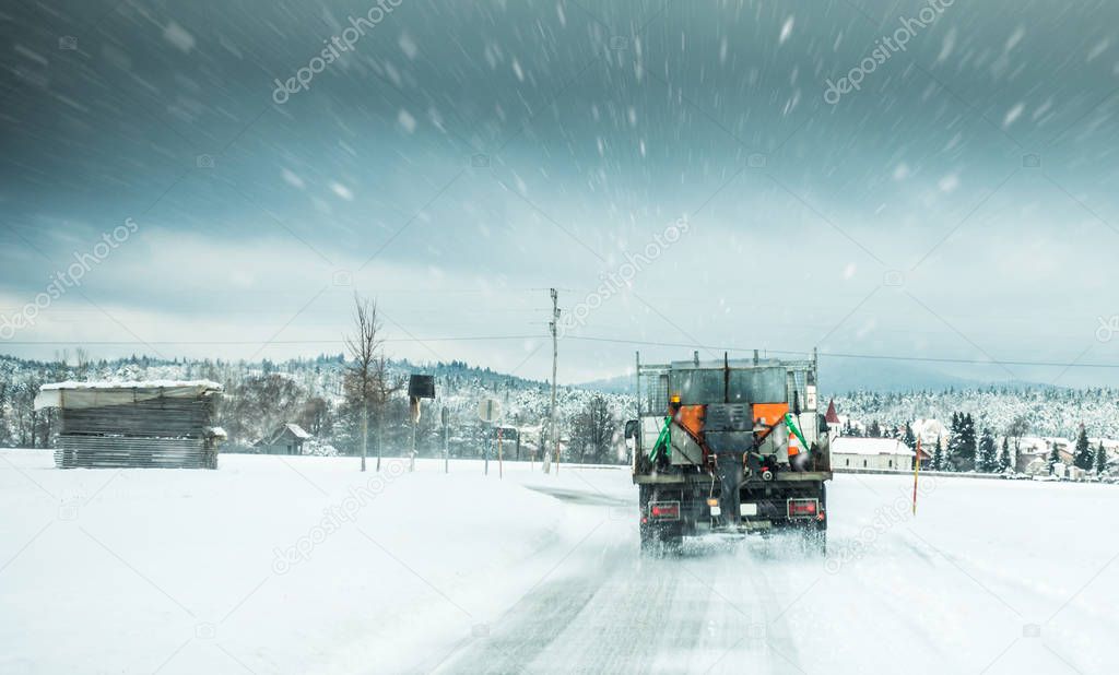 Winter service truck or gritter spreading salt on the road surface to prevent icing in stormy snow winter day. 