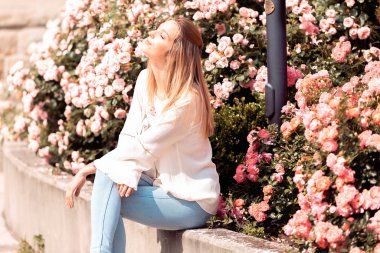 Sarışın kadın çiçeklerin yanında güneşleniyor.