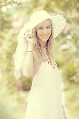 Bulanık bahçe arka planında poz veren şapkalı sarışın kadın.